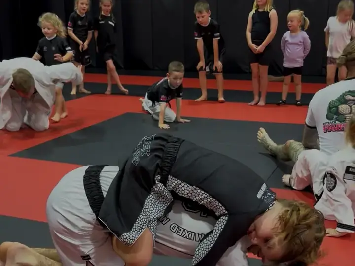 A coach teaching a group of children a grappling position in the kids class
